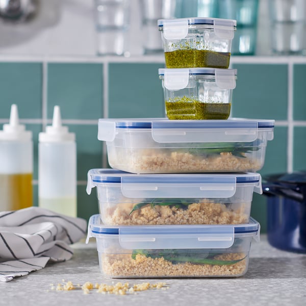Sakrauti caurspīdīgi plastmasas pārtikas trauki ar slēdzenēm uz letes, daži piepildīti ar graudiem un garšaugiem. IKEA 365+ zīmols.