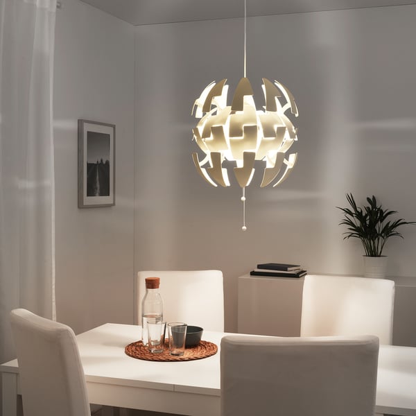 Balta IKEA PS 2014 piekaramā lampa virs ēdamgalda, kas rada maigu mirdzumu.
