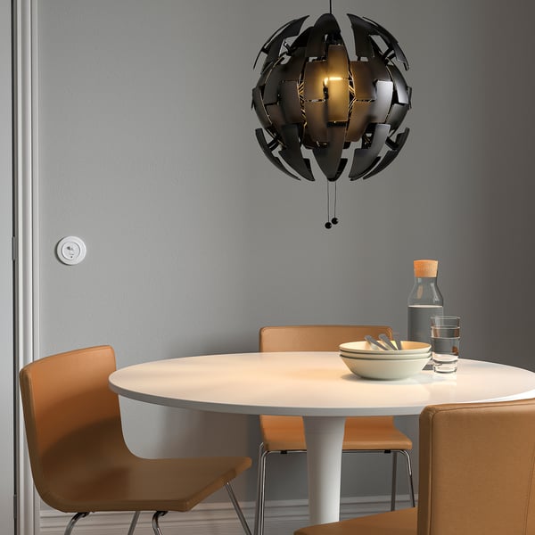 Mūsdienīgs ēdamistabas komplekts ar IKEA PS 2014 melnu piekaramo lampu, oranžiem krēsliem un galdu ar bļodu, glāzēm un pudeli.