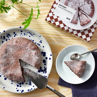 Attēlā redzama šokolādes kūka ar marķējumu KAFFEREP, puse pasniegta uz šķīvja un puse iepakojumā, ar šķēli uz atsevišķa ēdiena, kas gatavs ēst.