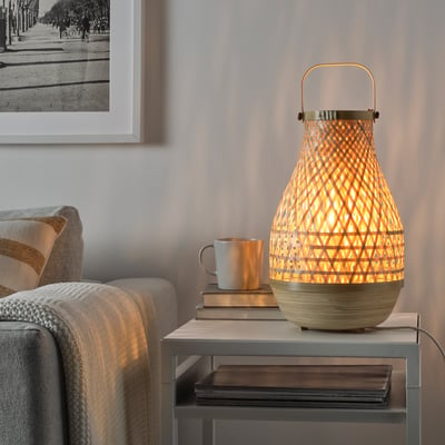 Mājīga viesistaba ar LUNNOM lampu, uzkodām un grāmatām uz galda pie pelēka dīvāna.