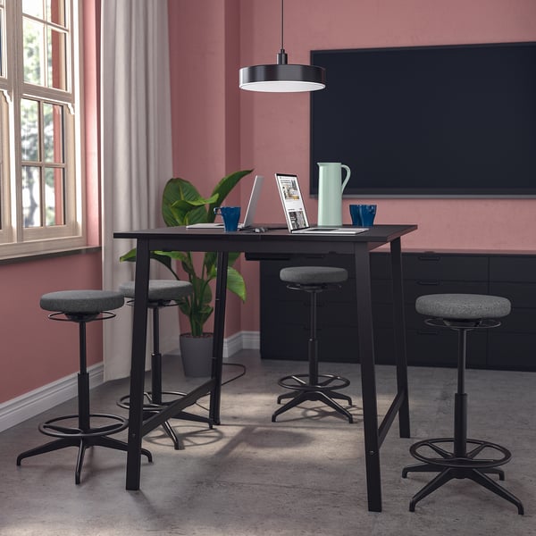 MITTZON augstais konferenču galds, melns, tērauds/koks, taisnstūrveida, ar četriem regulējamiem izkārnījumiem, podiņu, klēpjdatoru, krūzītēm un lielu ekrānu aiz muguras.