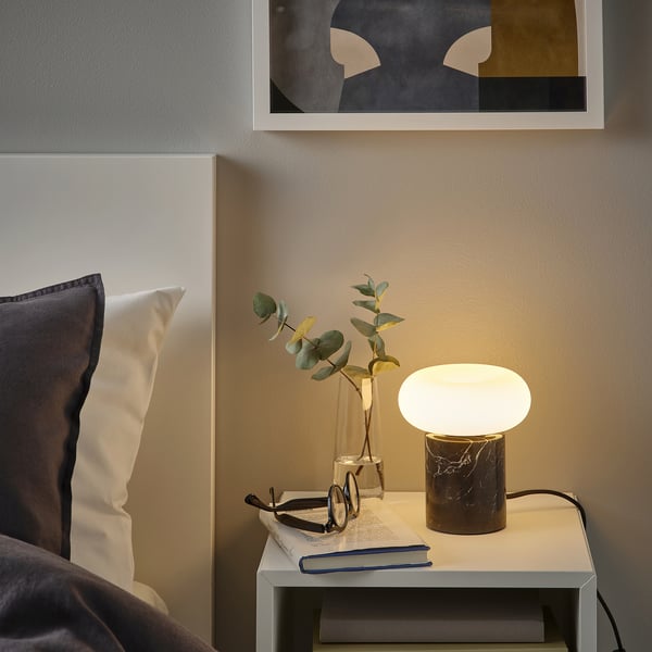 Stilīga guļamistaba ar MOLNART lampu, augiem, grāmatu un abstraktu mākslu.