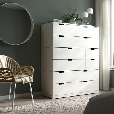 Balta NORDLI kumode guļamistabā; garš, plats ar vairākām atvilktnēm, netālu no pīta krēsla un liela spogulis.
