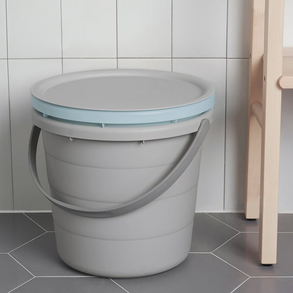 Pelēks plastmasas PEPPRIG spainis ar gaiši zilu vāku un rokturiem atrodas uz flīžu grīdas. Vāka blīvējumi uzglabāšanai.