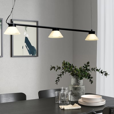 Mūsdienīga ēdamistabas zona ar SAMBORD lampu virs galda komplekta ar glāzēm, šķīvjiem un apstādījumiem. Gluds, minimālisma dizains ar plašu gaismu.