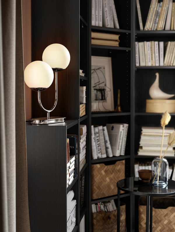 Mūsdienīgs lampa ar diviem baltiem stikla globusiem melnā plauktā.