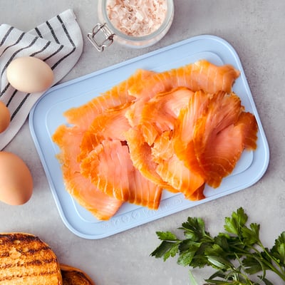 Zilā paplāte uz letes tiek turēts sagriezts, kūpināts lasis starp citiem pārtikas produktiem.