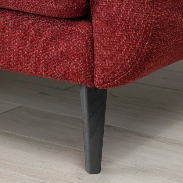 Sarkana spilvena dīvāna tuvplāns ar koka kājām, kas demonstrē kvalitatīvu polsterējumu un izturīgu dizainu.