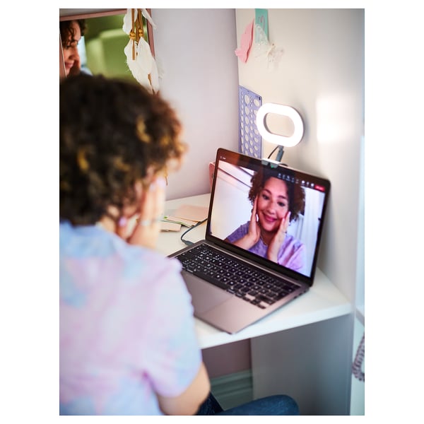 Persona ar cirtainiem matiem videozvanā, smaida klēpjdatoram ar pievienotu gredzena gaismu.