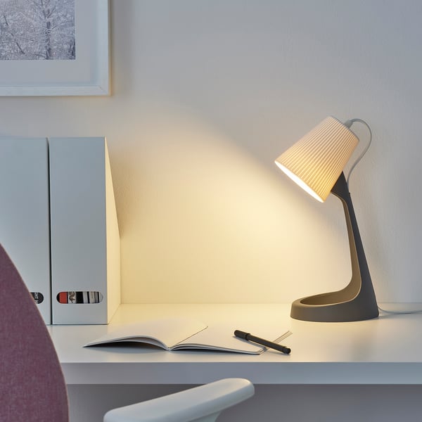 Mūsdienīga SVALLET lampa uz biroja galda ar piezīmjdatoru, mapi un monitoru. Sienai ir ierāmēts attēls.