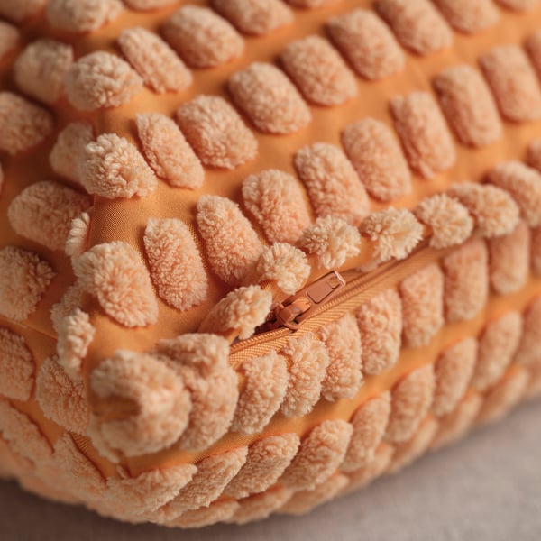 Mīksts, teksturēts oranžs spilvena pārvalks ar redzamu rāvējslēdzēju.