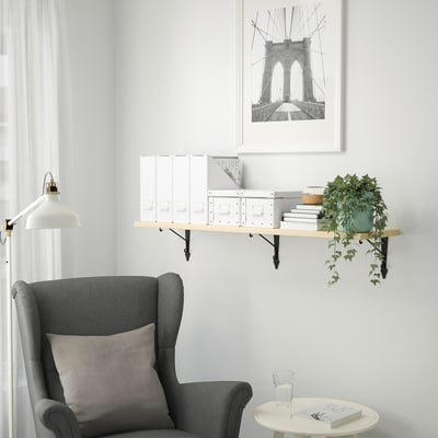 Minimālisma lasīšanas stūrītis: pelēks krēsls, peldošs plaukts ar baltu dekoru, piekaramais augs, Bruklinas tilta māksla.
