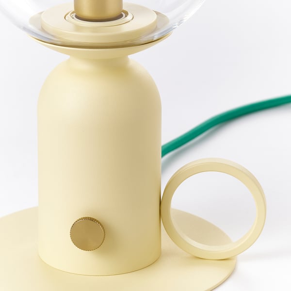 Светильник с золотым цоколем со стеклянным абажуром и зеленым шнуром.