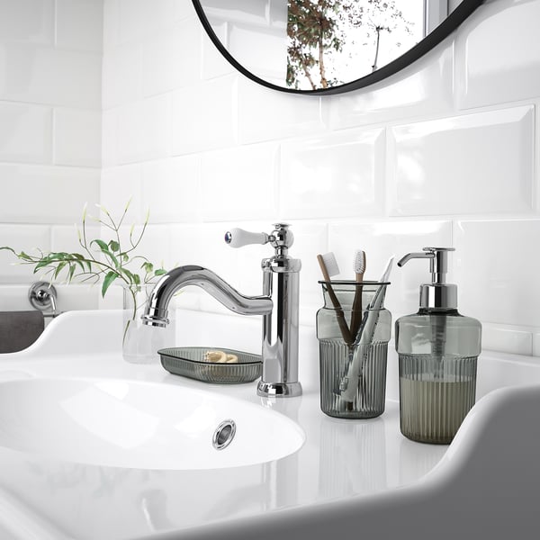 Современная раковина в ванной комнате с хромированным смесителем, дозатором зеленого мыла и поддоном. Минималистичный дизайн.