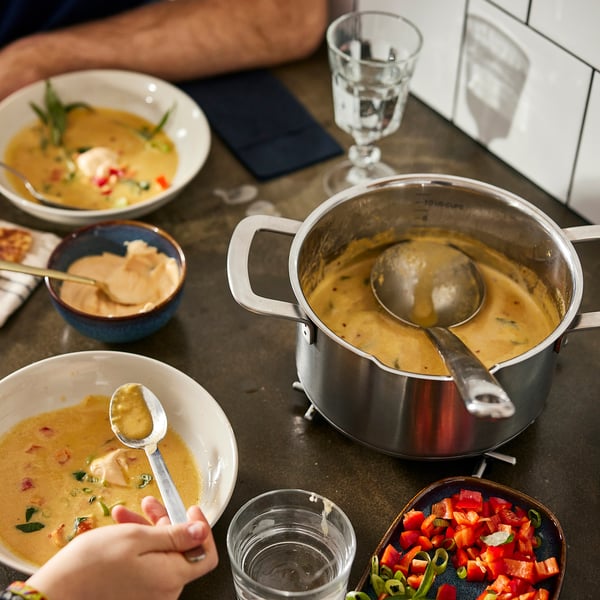 Суп на плите с тарелками и овощами рядом.