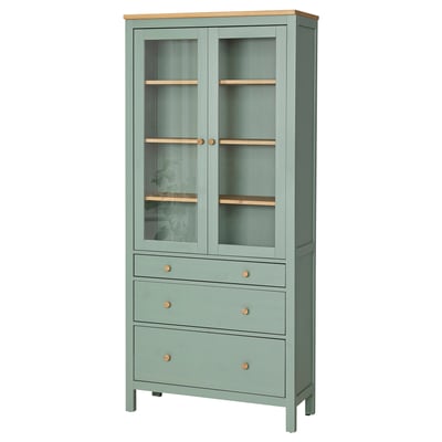 Зеленый шкаф HEMNES со стеклянными дверцами и деревянными вставками, выдвижными ящиками и регулируемыми полками.