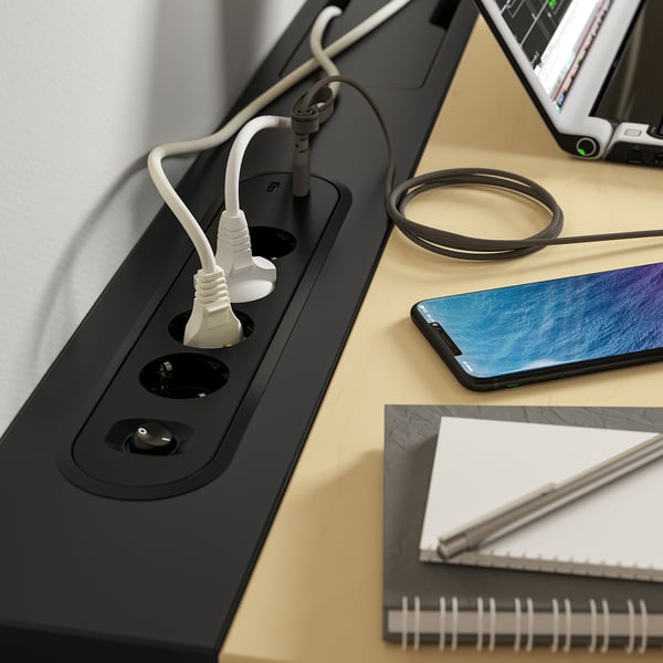 Письменный стол с розетками и usb-портами. Видны кабели для зарядки, телефон и ноутбук.