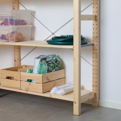 Полки для хранения из светлого дерева с прозрачными контейнерами с красочными предметами, в том числе зеленым шлангом и полиэтиленовыми пакетами на нижней полке.