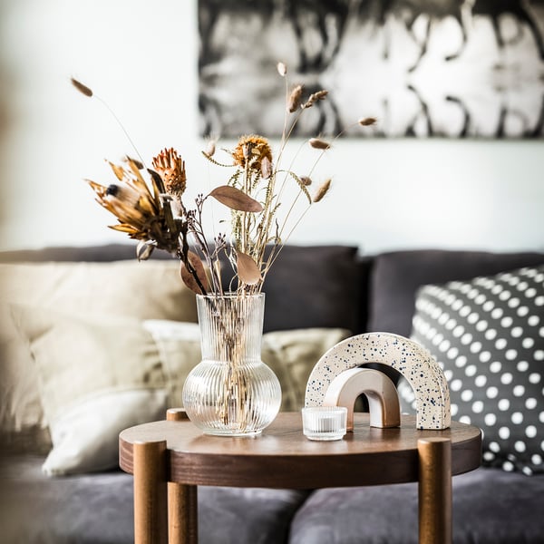 Гостиная с вазой PÅDRAG, сухоцветами, радужным декором, свечой и диваном с подушками.