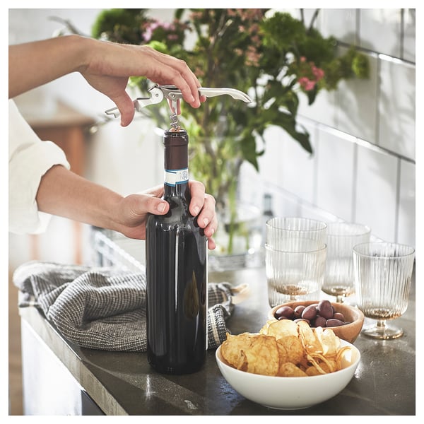 Открытие вина штопором SEGELFISK. На столе есть бокалы, закуски и цветы.