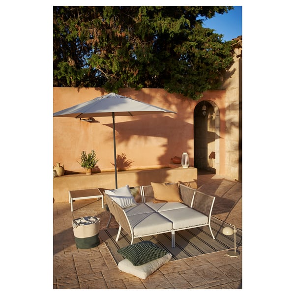 Места для отдыха на свежем воздухе с шезлонгами SEGERÖN, подушками, зонтом, синей корзиной и растениями.