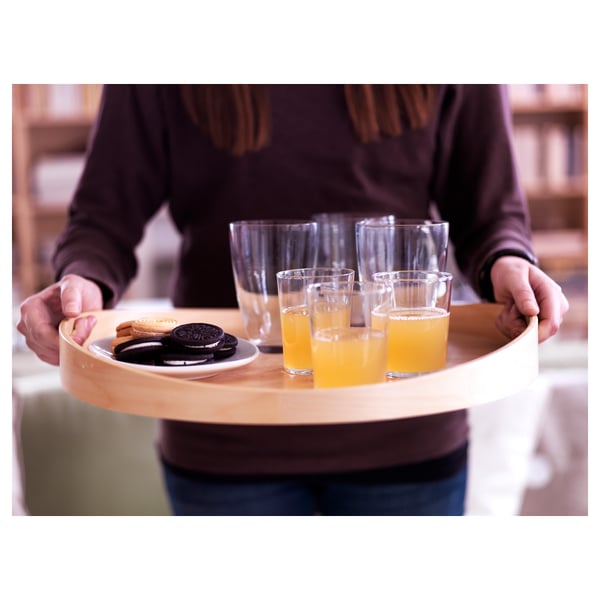 Человек несет березовый поднос со стаканами и печеньем.