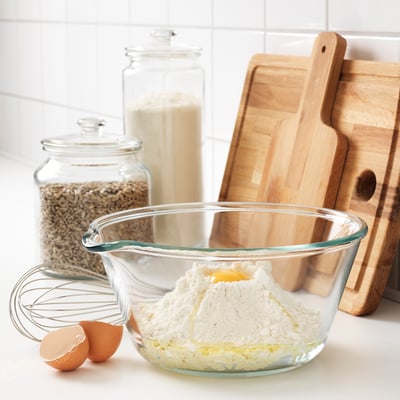 Стеклянная миска для смешивания с мукой и яйцом, деревянные разделочные доски, банки с зернами и мукой, а также венчик на прилавке, идеально подходит для выпечки.
