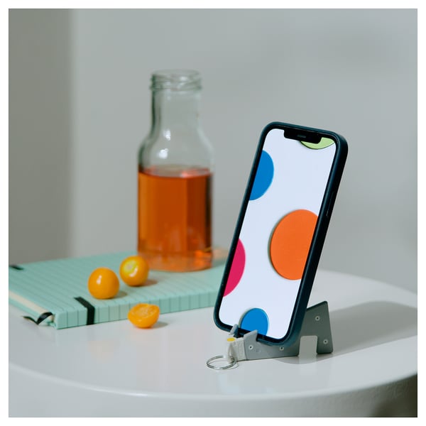 Черно-серый держатель для телефона с точками, на белом столе с напитком и фруктами.