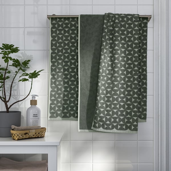 Green patterned towel hangs on metal bar, next to plant and hand cream on vanity in clean bathroom.