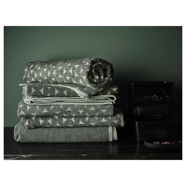 Three stacks of grey/green patterned towels on dark wood.