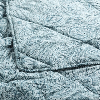 Blue and white paisley patterned duvet, lightly crumpled, showcasing intricate floral designs on a white background.
