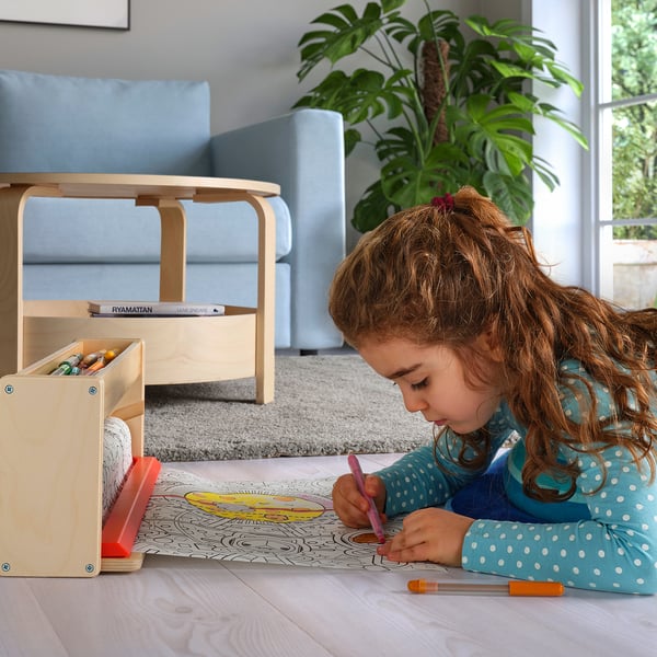 Child colouring on long paper roll, using crayons from wooden box.