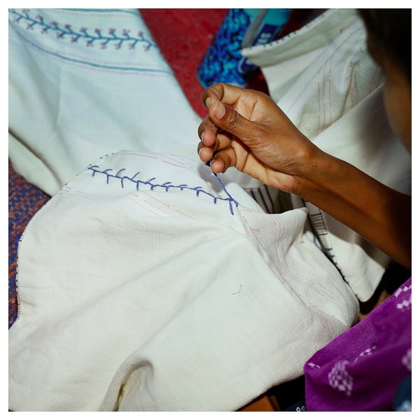 Embroidering white cushion with blue patterns, showcasing floral designs & traditional craftsmanship.