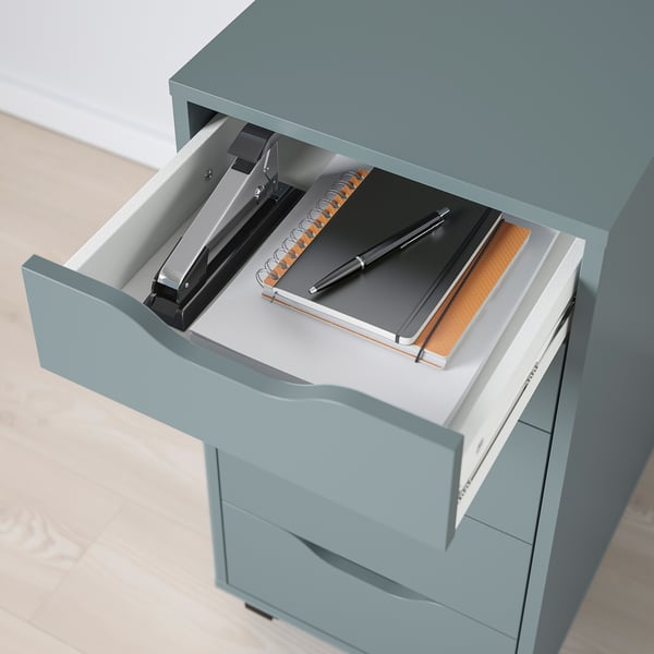 A green filing cabinet with a drawer open, revealing a stapler, notebook, and pen. Ideal for organised workspace.