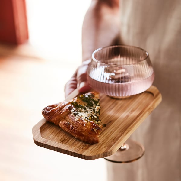 Person holding wooden tray with pastry and glass.