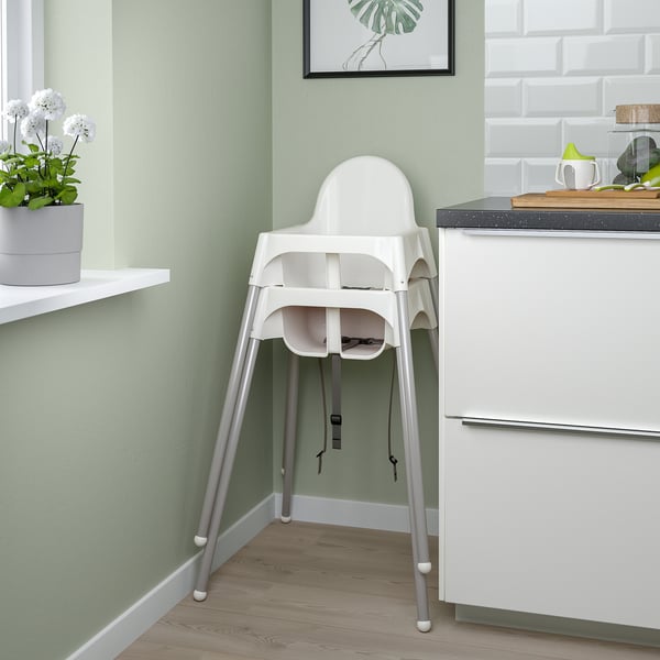 A white high chair positioned near a kitchen counter with green walls, featuring a safety belt, easy to disassemble.