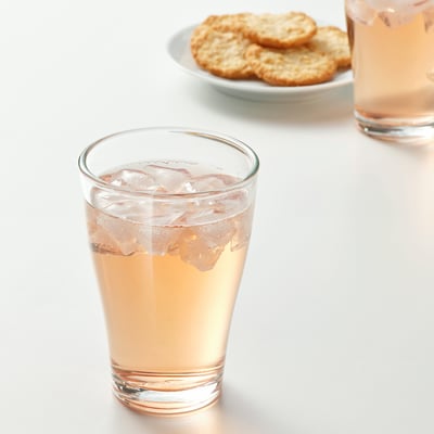 A glass filled with a light-colored drink and ice sits next to a plate of crackers. The glass is designed to stack easily, saving space.