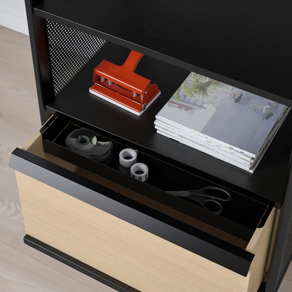 Black office storage unit with open drawer revealing a red stapler, stack of paper, sticky notes, scissors, and tape.