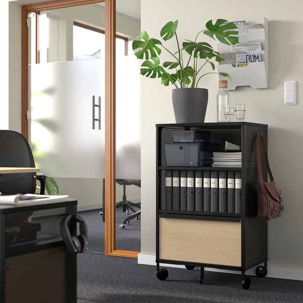 Modern office: black BEKANT storage unit with plant, desk, chair, posters, and bag.