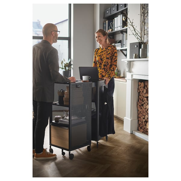Two people near BEKANT storage. Person types, person smiles. Bright room with fireplace.