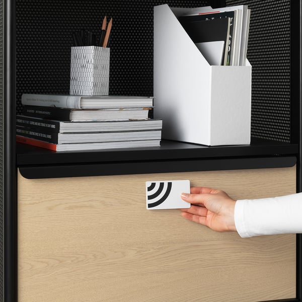 Person locking drawer with smart key under desk with books and office supplies.