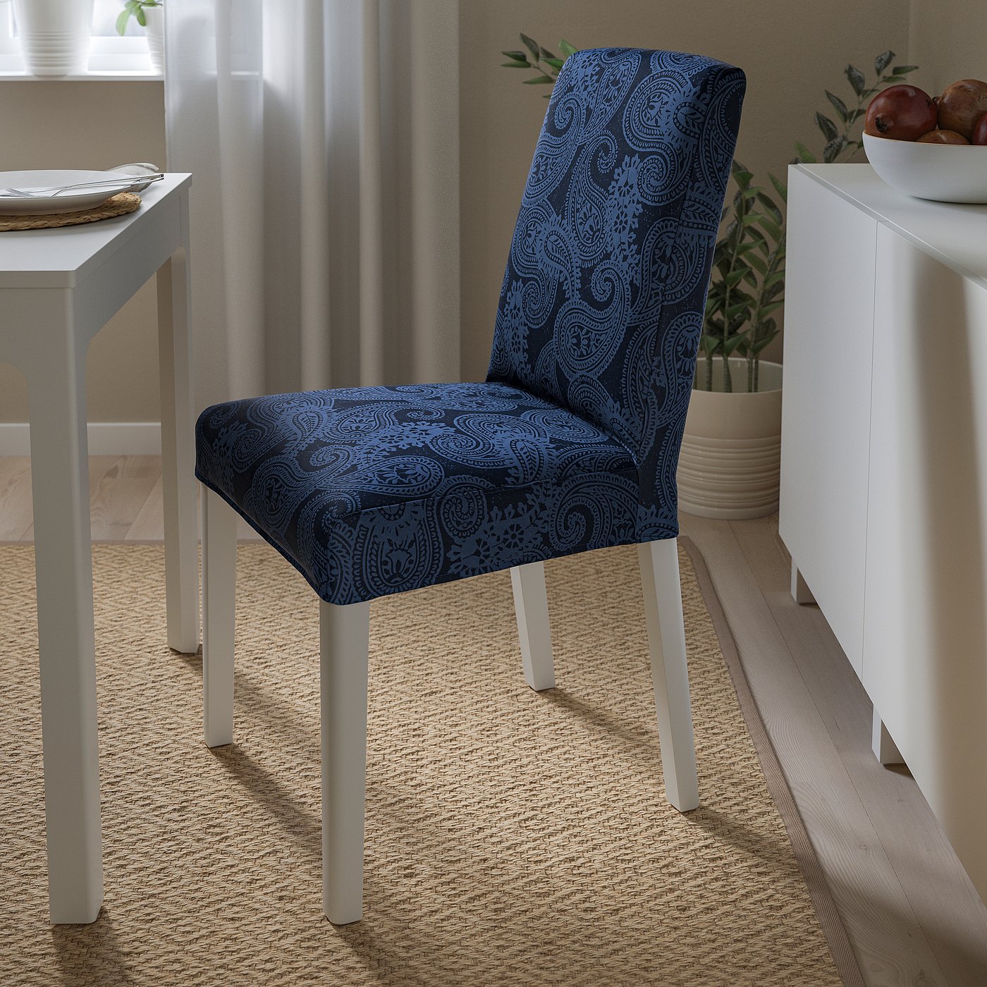 Blue paisley-printed chair cover with white legs, positioned next to a white cabinet and a small dining table with a bowl of fruit.