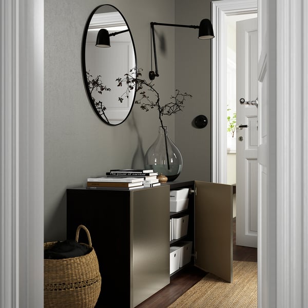 Modern entrance: opened storage unit with open door, mirror, vase, books, light fixtures.