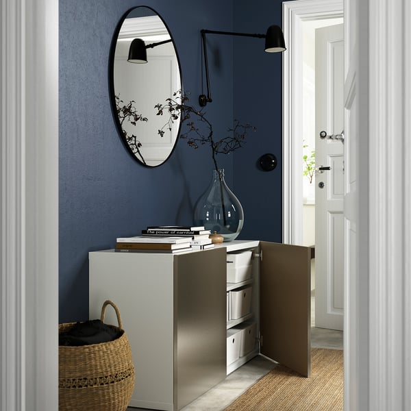 A hallway with a BESTÅ storage unit. It has adjustable shelves, soft-closing doors, and a surface with books and a vase.