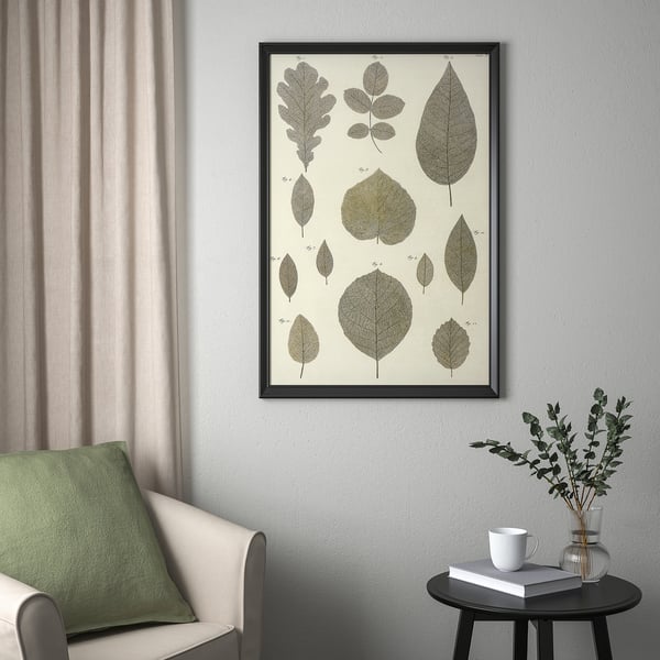 Modern living room with BILD poster, leaf designs, beige curtains, white armchair, green cushion, side table with book, mug, and eucalyptus.