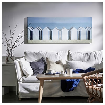 Cosy living room with white couch, low wooden table, and BJÖRKSTA canvas of beach huts.