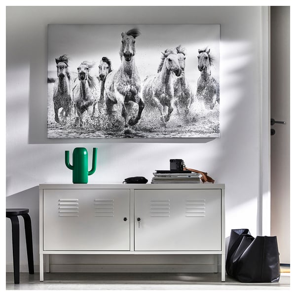 Large wall art featuring horses, above a metal locker unit. Includes a green decorative cactus and books on top of the locker.