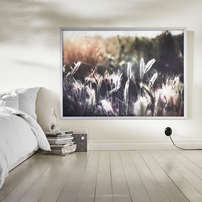 Large wall art in white and grey tones, featuring grassy landscape. Framed in white aluminium, displayed above wooden floor with white bed.