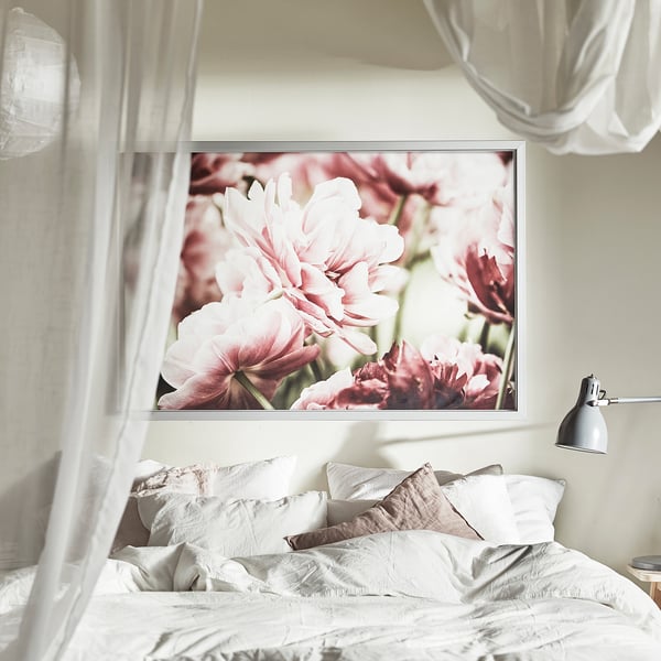 Bedroom with large floral framed art above bed; white linens, lamp.